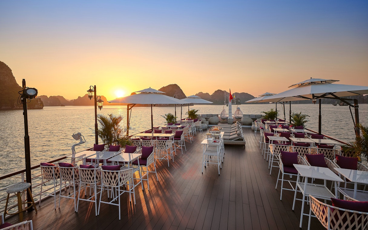 Sundeck with tables and chairs overlooking a sunset on Halong Bay, Vietnam.