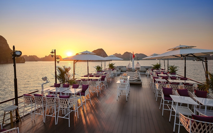 Sundeck with tables and chairs overlooking a sunset on Halong Bay, Vietnam.