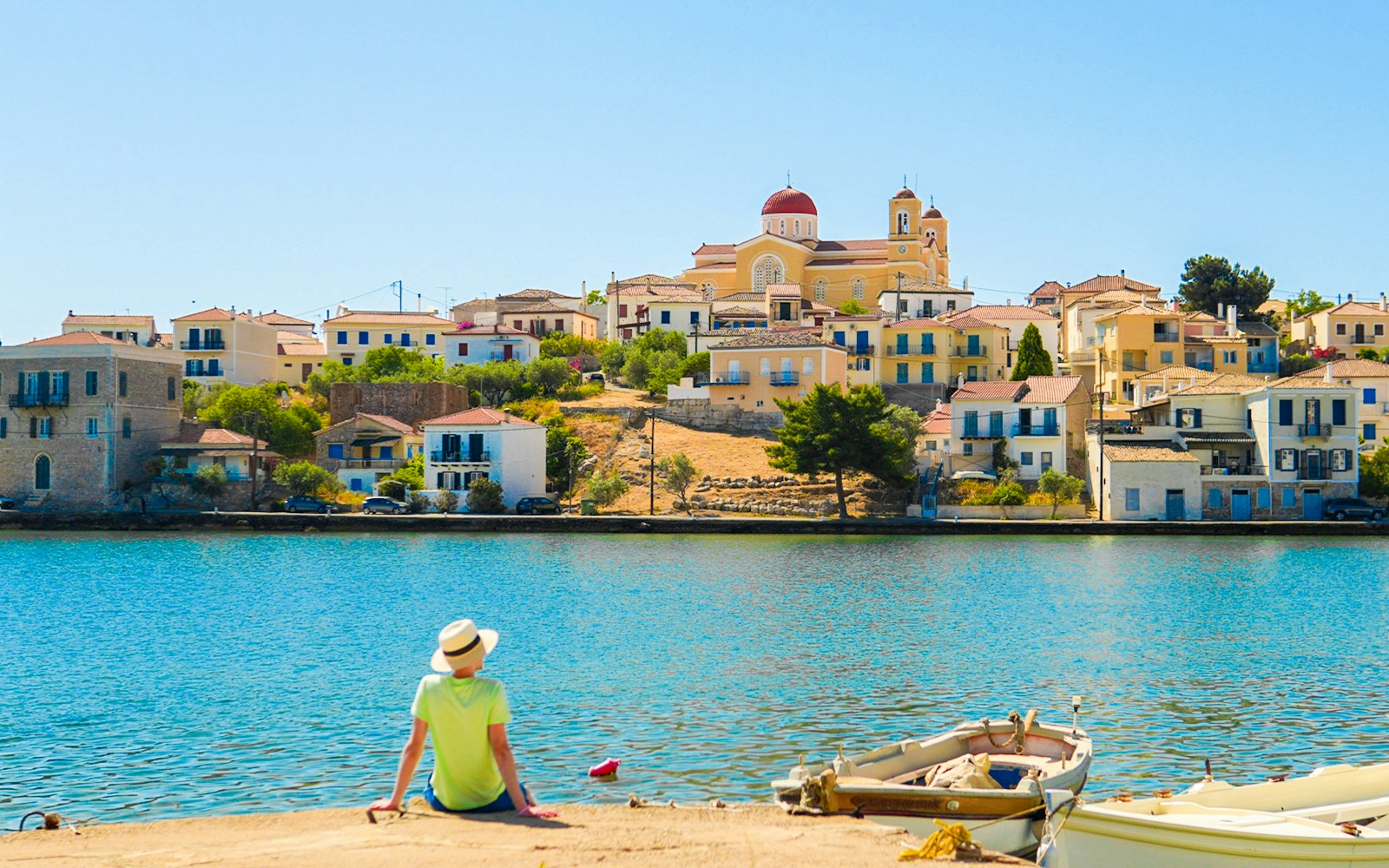 Man sitting by the water with a view of Galaxidi, Greece houses and church.