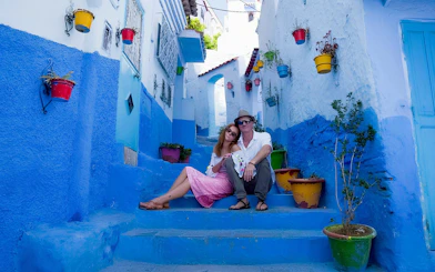 Couple sitting on blue steps in Chefchaouen, Morocco with colorful pots.