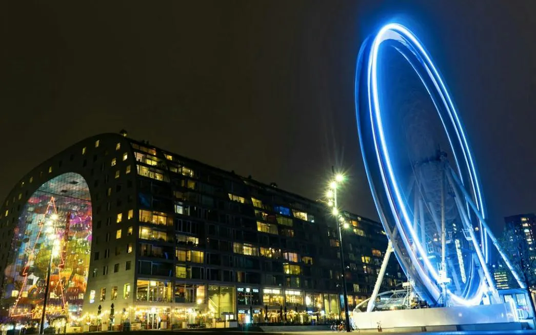 Rotterdam Markthal and illuminated Ferris wheel at night during city exploration game.