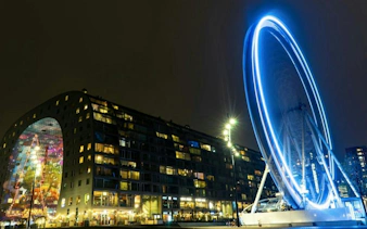 Rotterdam Markthal and illuminated Ferris wheel at night during city exploration game.