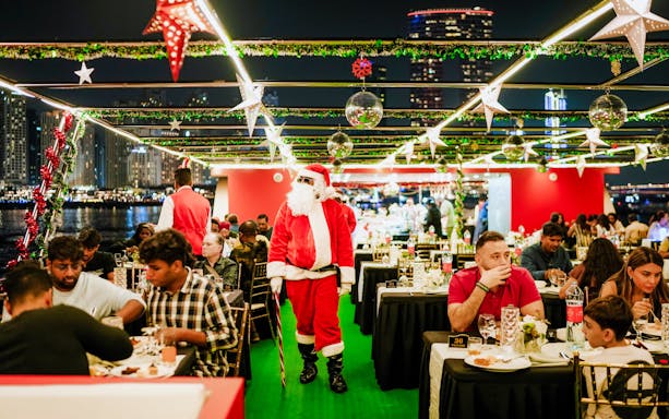 Santa Claus walking through a festive dinner cruise with guests enjoying an international buffet.