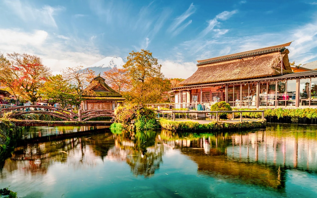 Traditional Japanese buildings by a pond at Oshino Hakkai, with Mount Fuji in the background.