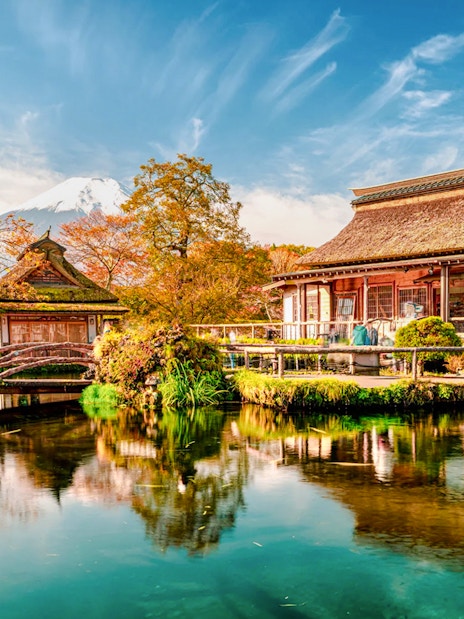 Traditional Japanese buildings by a pond at Oshino Hakkai, with Mount Fuji in the background.