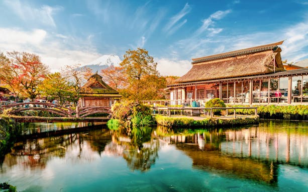 Traditional Japanese buildings by a pond at Oshino Hakkai, with Mount Fuji in the background.