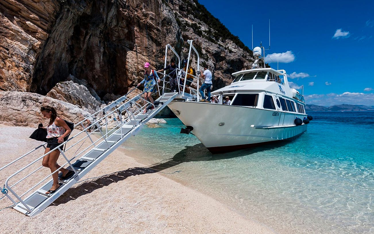 Passengers disembarking from a boat on a sandy beach during a Gulf of Orosei mini cruise from Cala Gonone.
