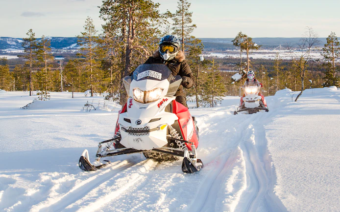 Snowmobiles racing through snowy forest in Rovaniemi, Finland.