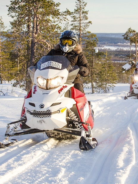 Snowmobiles racing through snowy forest in Rovaniemi, Finland.