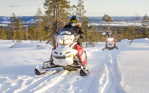 Snowmobiles racing through snowy forest in Rovaniemi, Finland.