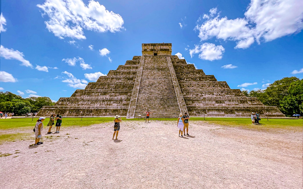 Chichen Itza pyramid with tourists exploring the site under a clear blue sky.