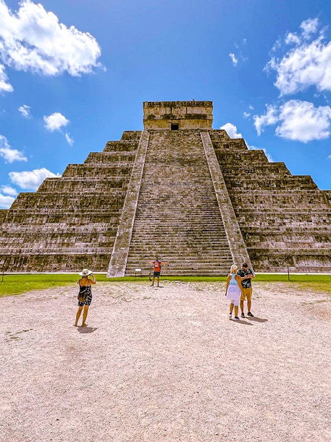 Chichen Itza pyramid with tourists exploring the site under a clear blue sky.