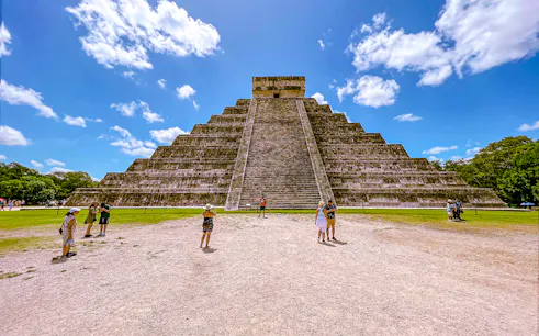 Chichen Itza pyramid with tourists exploring the site under a clear blue sky.