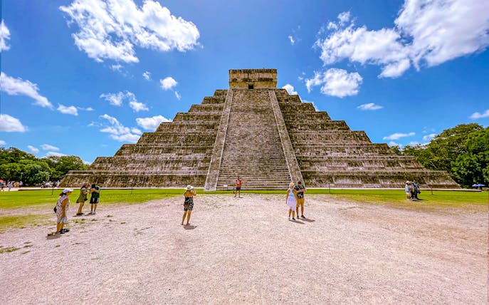 Chichen Itza pyramid with tourists exploring the site under a clear blue sky.