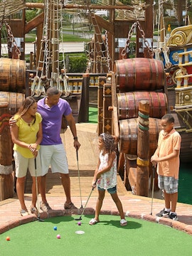 Family playing mini-golf at Pirate's Cove Adventure Golf with pirate ship backdrop.