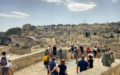 Tourists overlooking Matera's ancient cityscape with stone buildings and sculptures.
