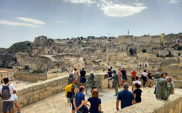 Tourists overlooking Matera's ancient cityscape with stone buildings and sculptures.