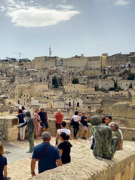 Tourists overlooking Matera's ancient cityscape with stone buildings and sculptures.