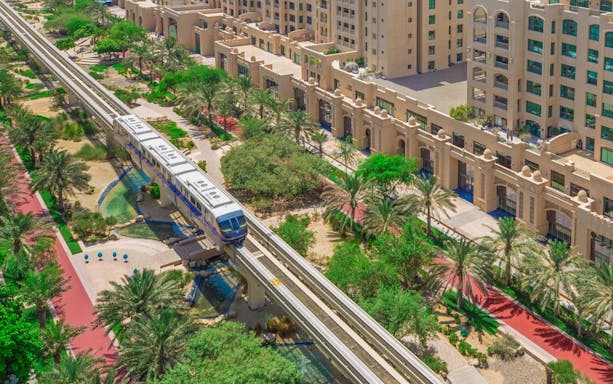 Palm Jumeirah Monorail passing through lush greenery and modern architecture in Dubai.