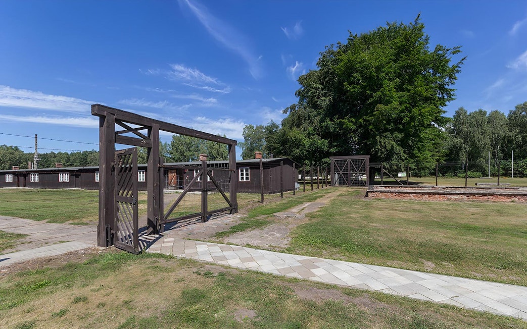 Stutthof Concentration Camp entrance gate and barracks under a clear blue sky.