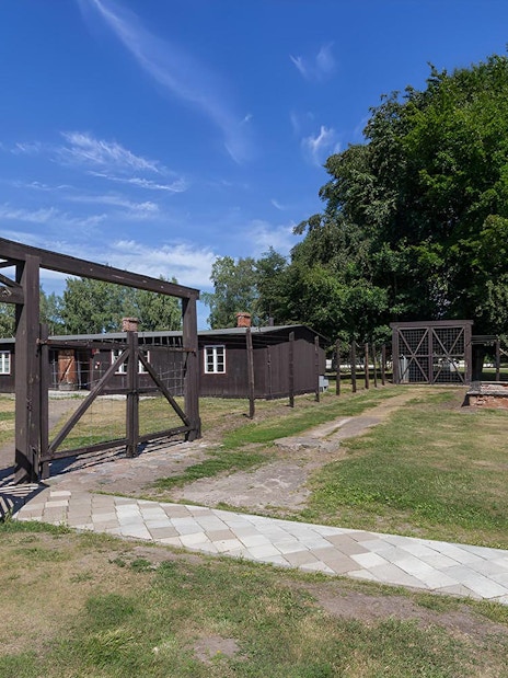 Stutthof Concentration Camp entrance gate and barracks under a clear blue sky.