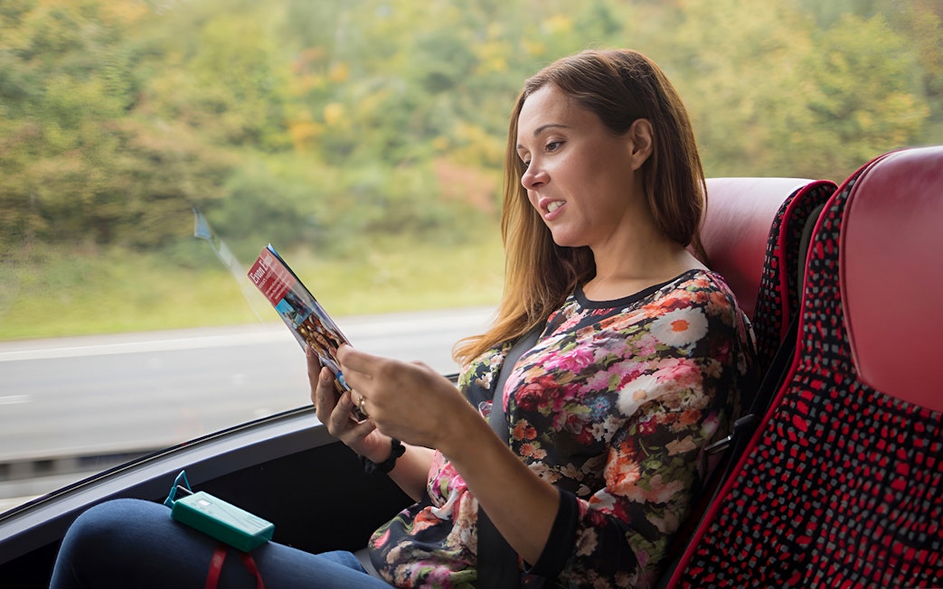 Person reading a brochure on a bus during a Stonehenge and Windsor tour from London.
