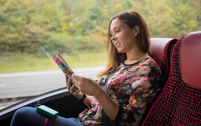 Person reading a brochure on a bus during a Stonehenge and Windsor tour from London.