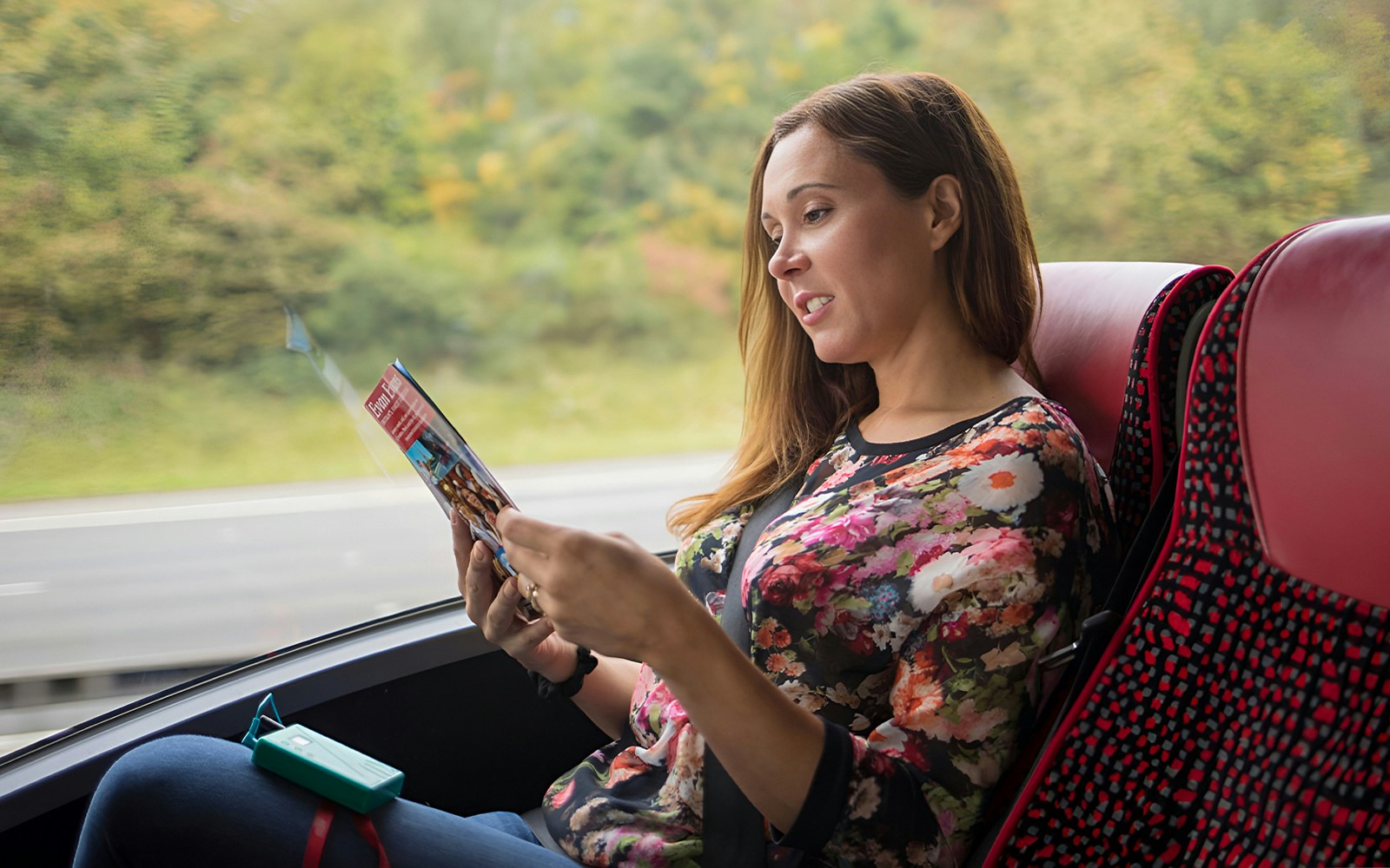 Person reading a brochure on a bus during a Stonehenge and Windsor tour from London.