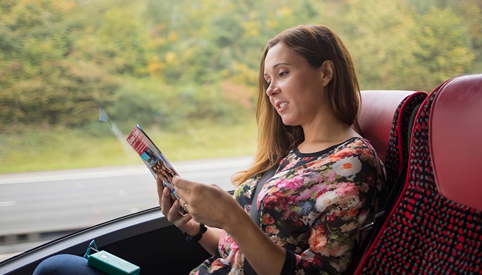 Person reading a brochure on a bus during a Stonehenge and Windsor tour from London.