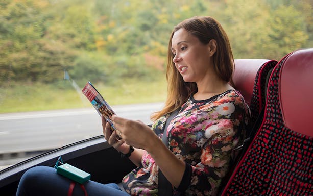 Person reading a brochure on a bus during a Stonehenge and Windsor tour from London.