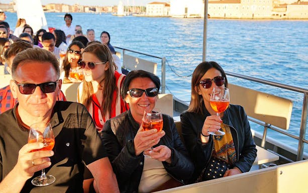 Tourists enjoying drinks on a boat during the Guided Sunset Panoramic Tour in Venice.