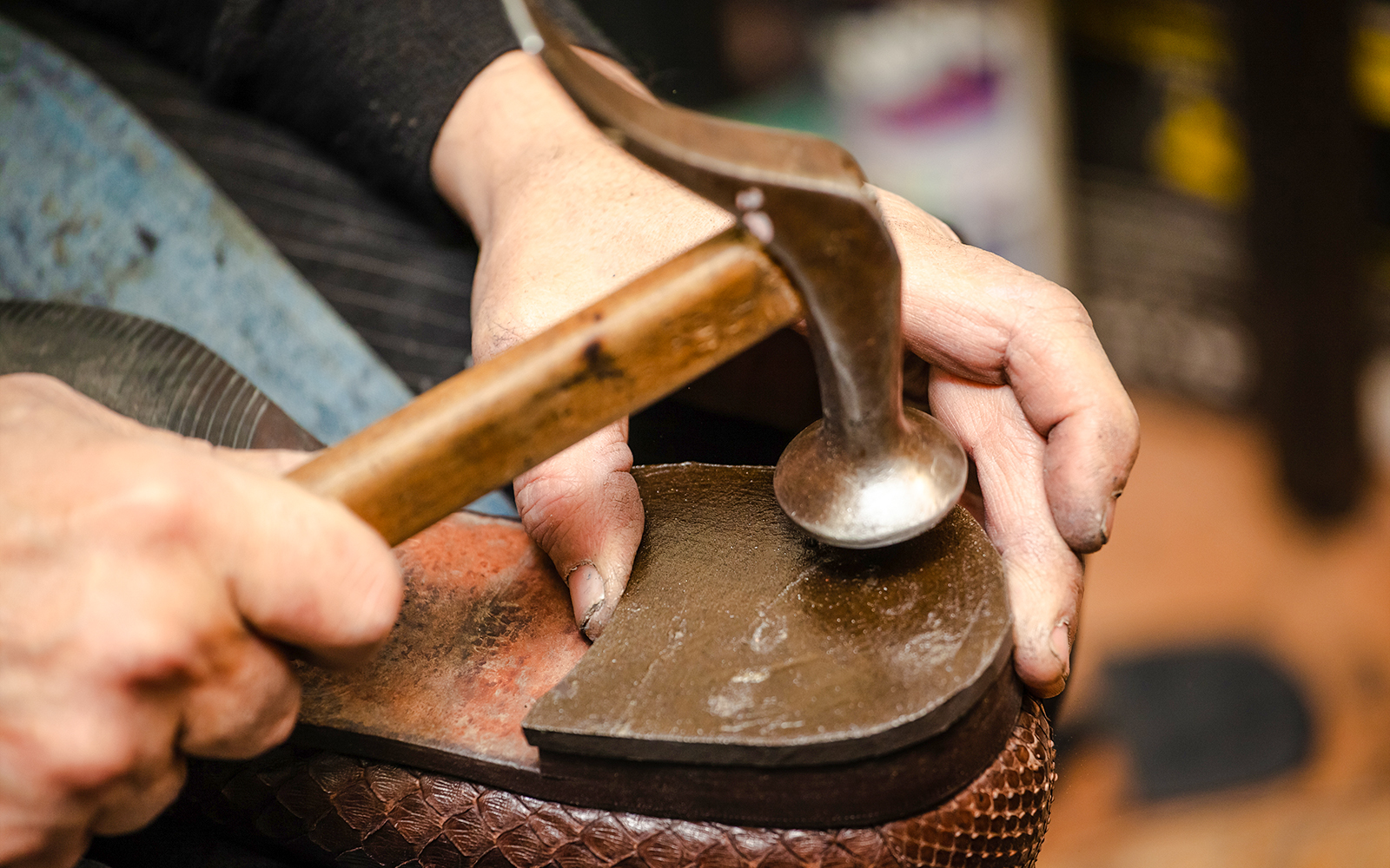 Shoemaker crafting a shoe sole with a hammer.