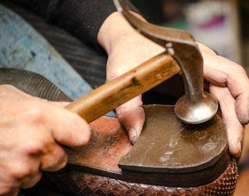 Shoemaker crafting a shoe sole with a hammer.