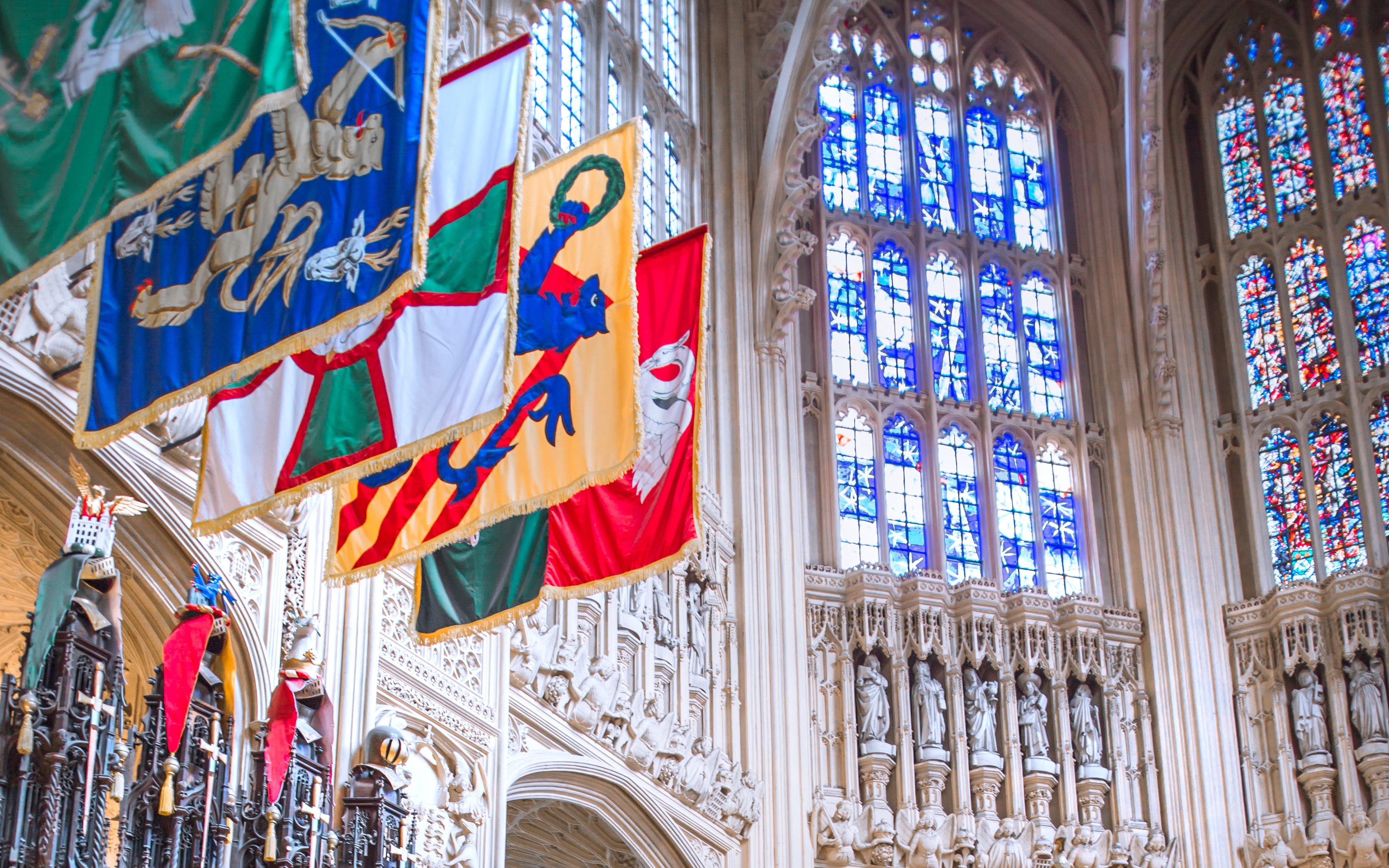 Heraldic banners hanging in a historic cathedral with stained glass windows.