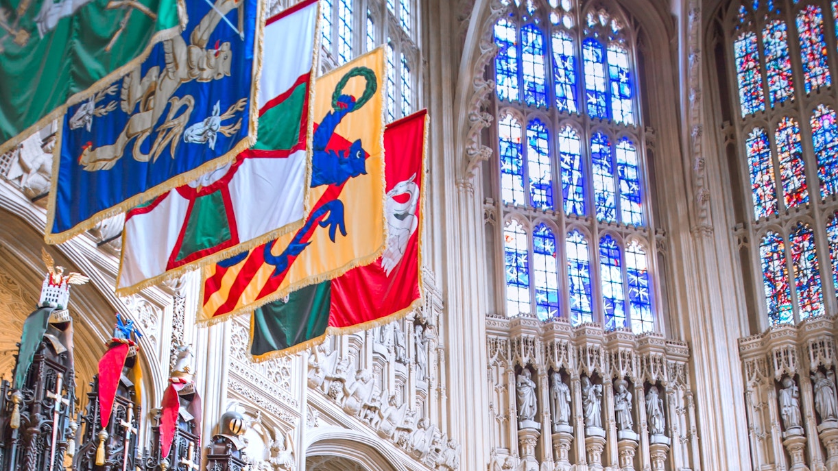 Heraldic banners hanging in a historic cathedral with stained glass windows.