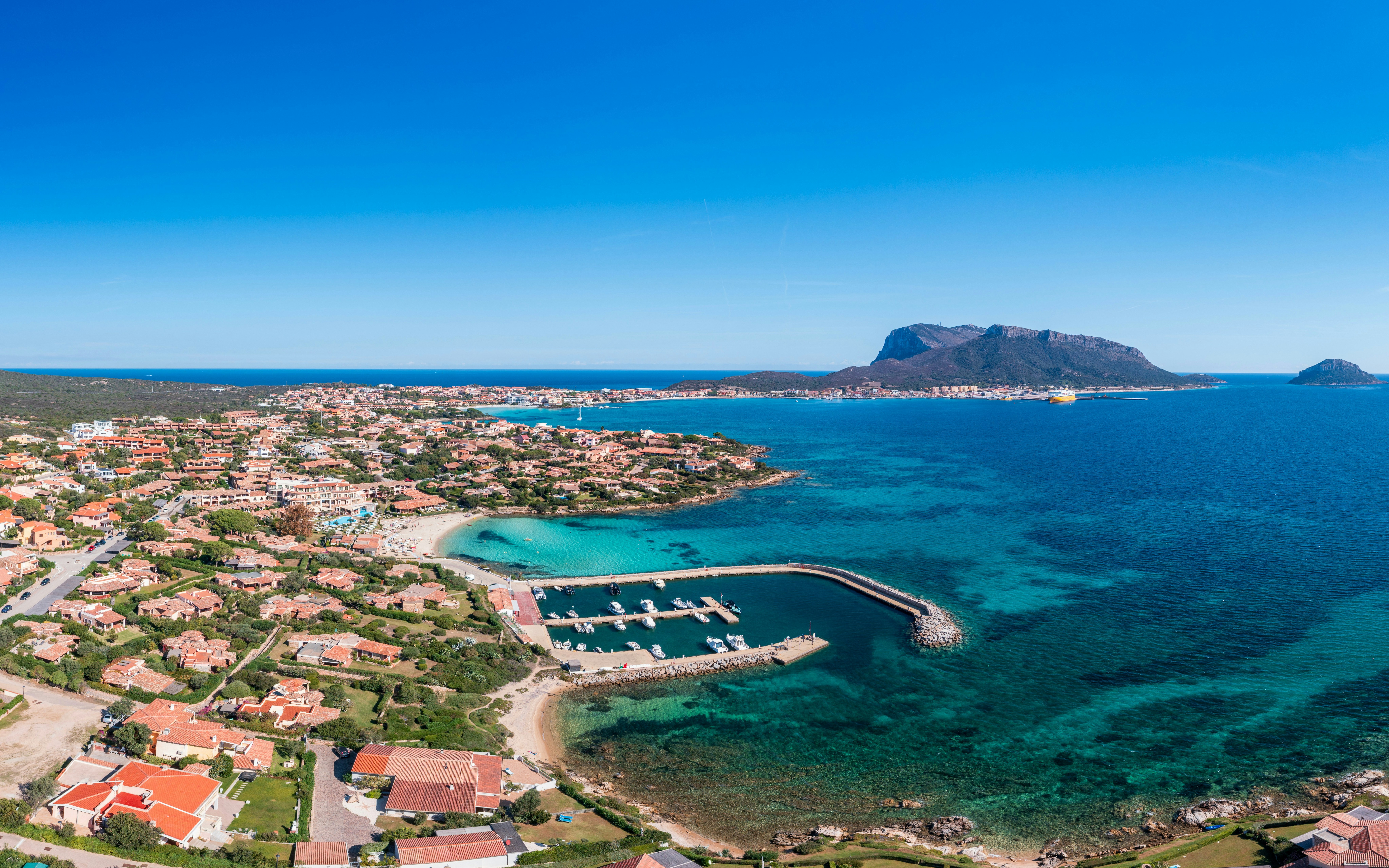 Aerial view of Golfo Aranci coastline with marina and turquoise waters in Sardinia, Italy.