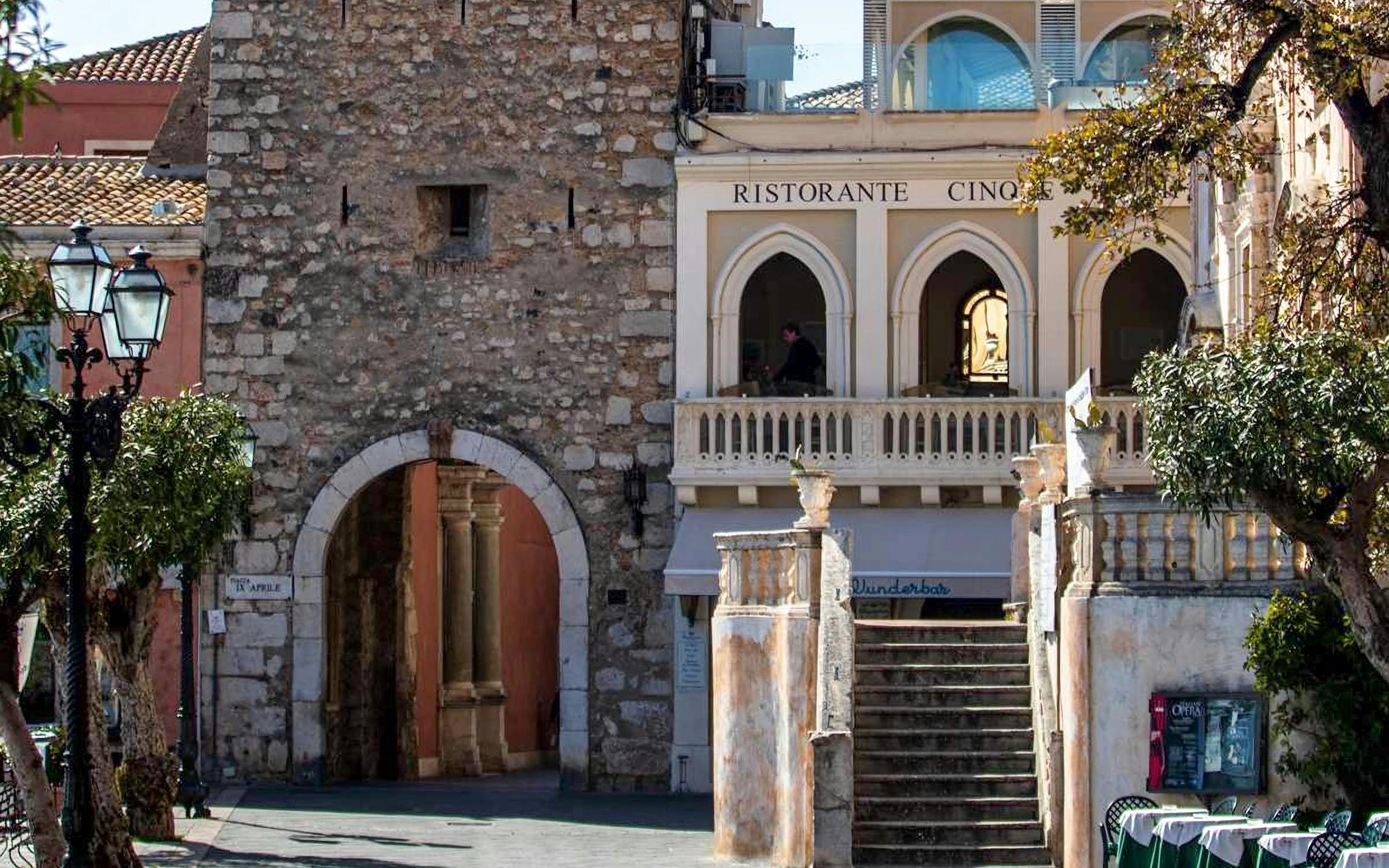 Torre dell'Orologio in Piazza IX Aprile, Taormina, with adjacent restaurant and stone archway.