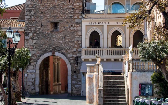 Torre dell'Orologio in Piazza IX Aprile, Taormina, with adjacent restaurant and stone archway.