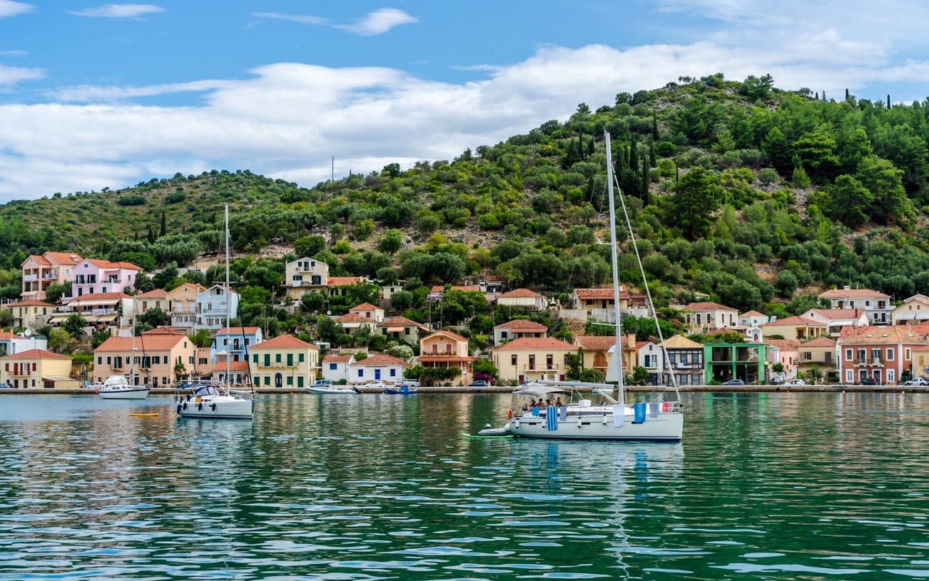 Sailboats in Vathi harbor with colorful houses and green hills, Greece.