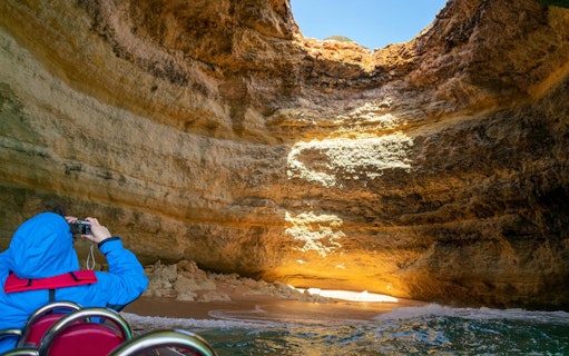 Tourist photographing inside Benagil Caves on RIB boat adventure, Algarve, Portugal.