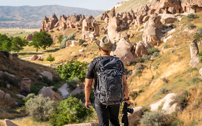 Photographer with camera at Zelve Open Air Museum, Cappadocia, overlooking rock formations.