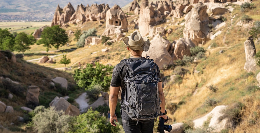 Photographer with camera at Zelve Open Air Museum, Cappadocia, overlooking rock formations.