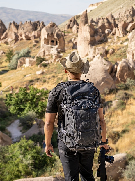 Photographer with camera at Zelve Open Air Museum, Cappadocia, overlooking rock formations.