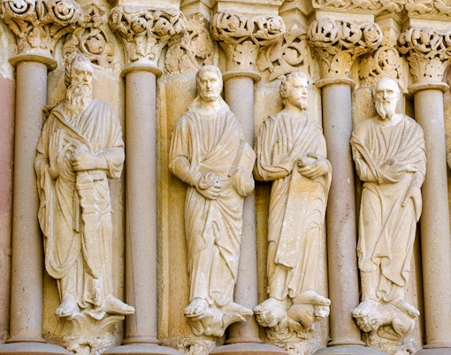 Stone sculptures of apostles on the facade of a Parisian cathedral, Assumption Day tour.