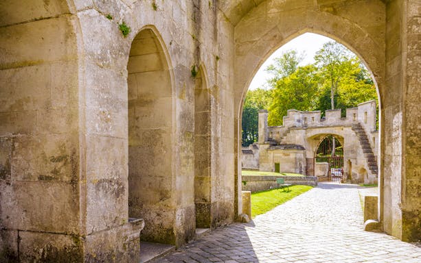 Arched stone entrance at Castle of Pierrefonds with cobblestone path and greenery.