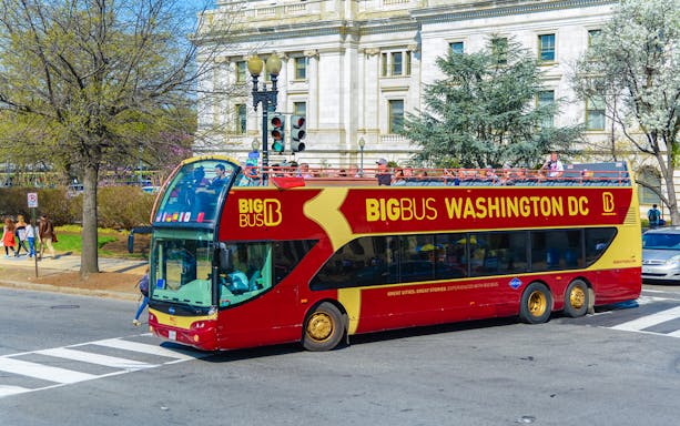 Open-top Big Bus tour in Washington DC passing a historic building.