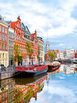 Amsterdam canal with historic buildings and boats reflecting in the water.