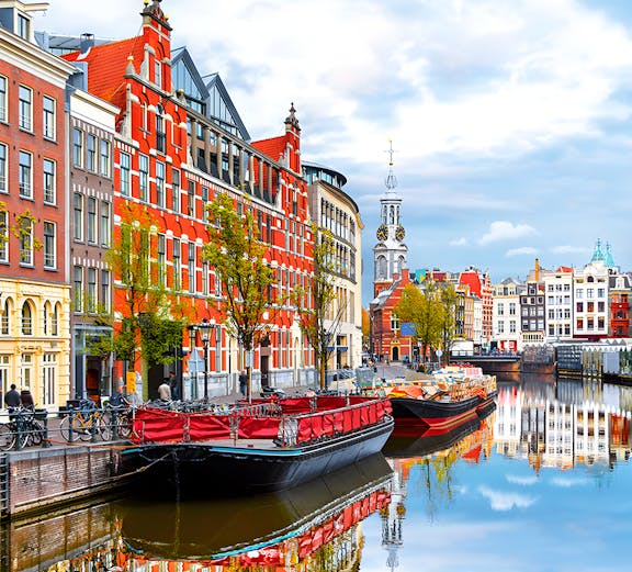 Amsterdam canal with historic buildings and boats reflecting in the water.