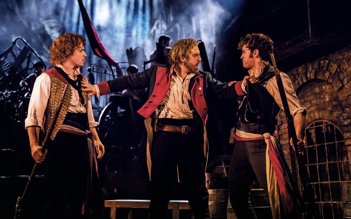 Actors in a dramatic scene from Les Miserables on stage.