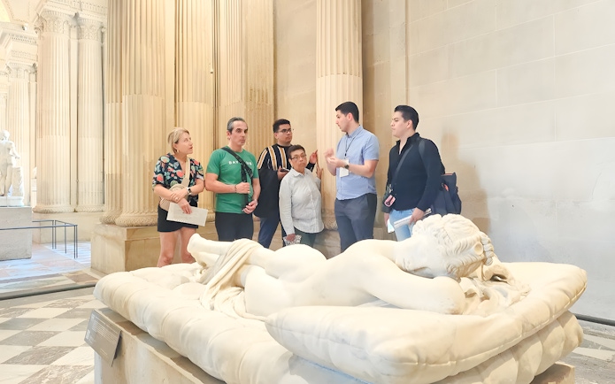 Group of people listening to a guide near a sculpture inside the Louvre Museum, Paris, France.